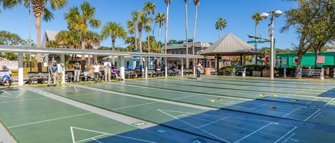 Ein Shuffleboard-Spielfeld im Freien mit überdachter Sitzgruppe und Palmen im Hintergrund.