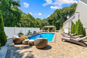 A backyard with a swimming pool, lounge chairs, and a covered patio area. - Retreat Luxury Home West Barnstable (Barnstable)