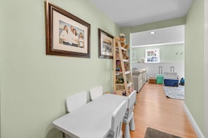 A room with a dining table, chairs, a bookshelf, a window, and a suitcase on the floor. - Retreat Luxury Home West Barnstable (Barnstable)