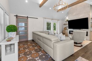 A modern living room with a sofa, a television, and a fireplace. - Retreat Luxury Home West Barnstable (Barnstable)