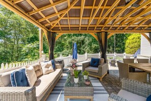 An outdoor patio with a pergola, wicker furniture, and a white fence. - Retreat Luxury Home West Barnstable (Barnstable)