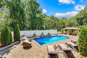 A backyard with a swimming pool, lounge chairs, and a covered seating area. - Retreat Luxury Home West Barnstable (Barnstable)