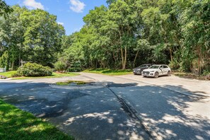A paved driveway with two cars parked on the side, surrounded by lush greenery and trees. - Retreat Luxury Home West Barnstable (Barnstable)