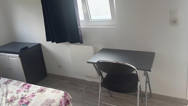 Una habitación con cama, escritorio, silla, ventana con cortinas y radiador.