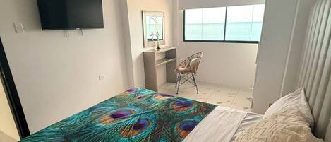 Un dormitorio con cama, televisión en la pared, una silla y ventana con vistas.