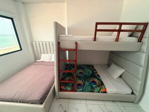 A bunk bed room with a window, a peacock-patterned bedspread, and a ladder.