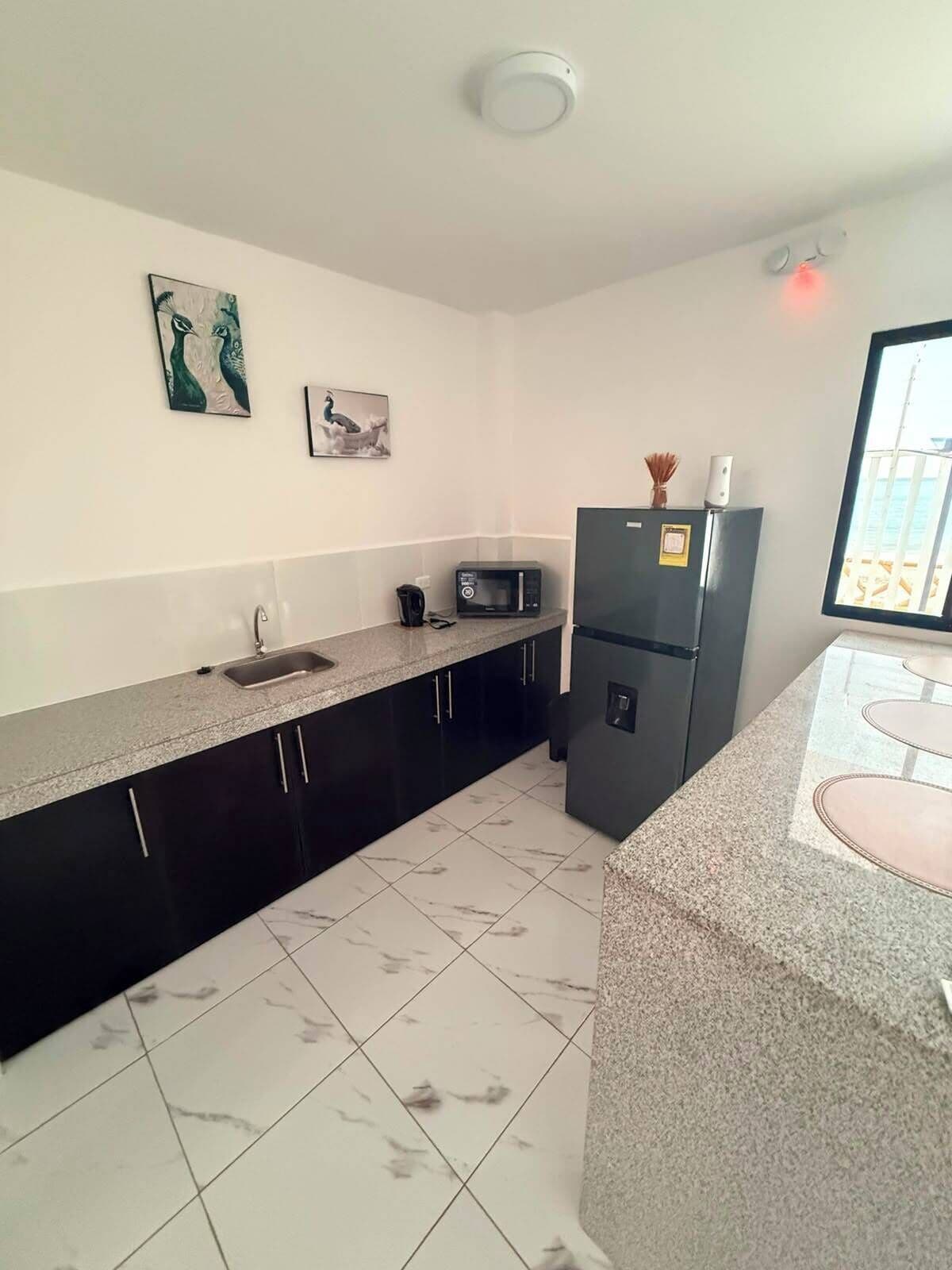 A kitchen with a marble floor, dark cabinets, a microwave, and a refrigerator.