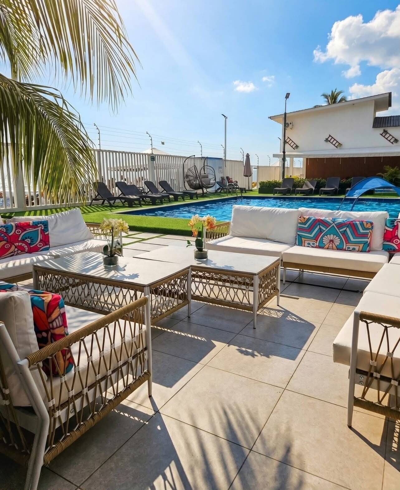 A poolside area with lounge chairs, a sofa, and a table with a vase of flowers.