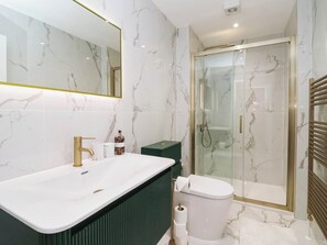 Ein modernes Badezimmer mit einer Marmorwand, einem weißen Waschbecken, einer grünen Kommode, einer Toilette und einer Duschkabine.