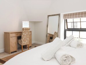 A bedroom with a bed, a wooden dresser, a chair, a mirror, and a window with curtains. - The Old Bakehouse (Beverley)
