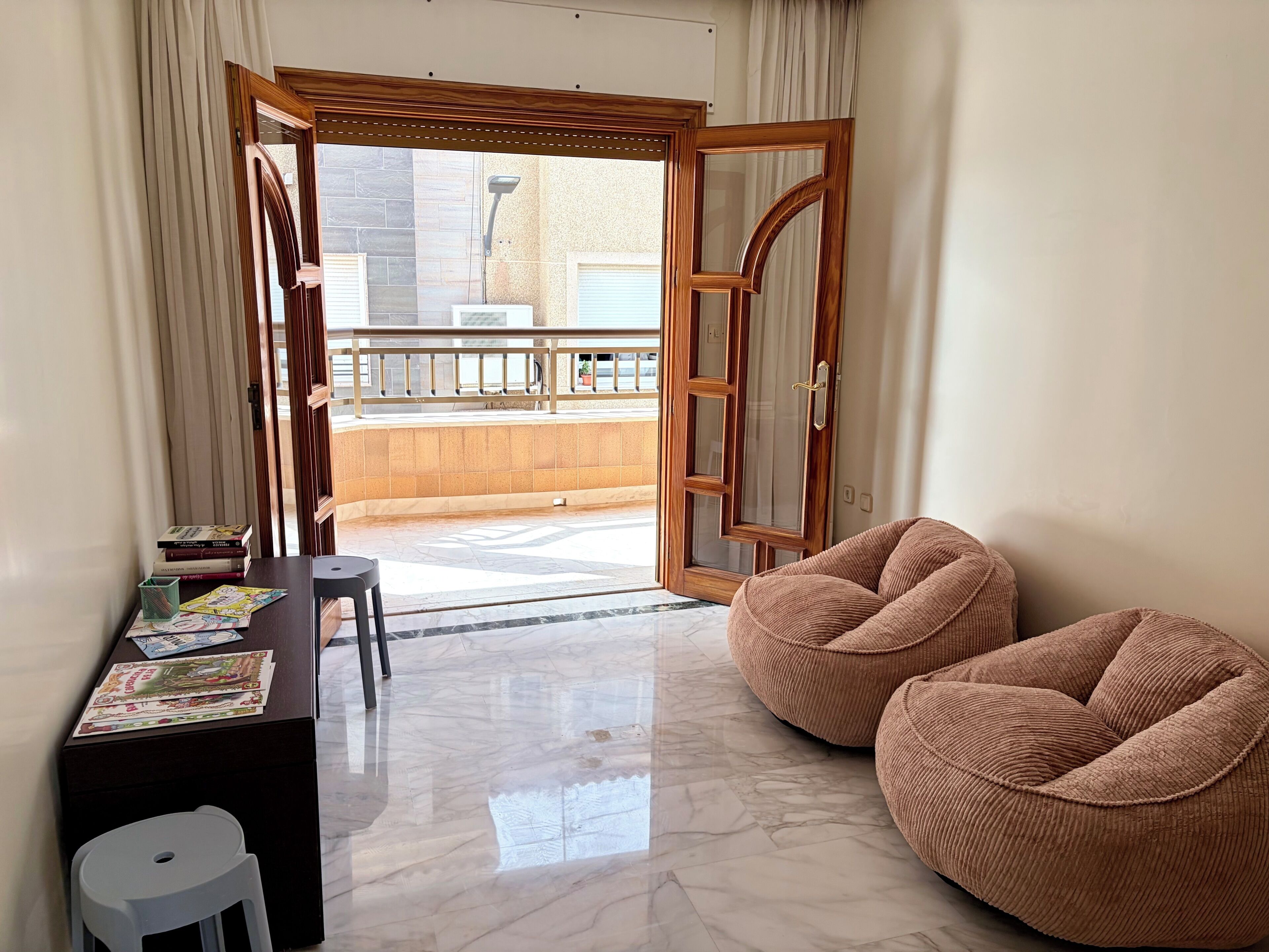 A room with a wooden door, a small table with books, a white stool, and two brown bean bag chairs.