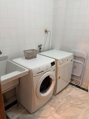 A compact laundry area with a washing machine, a sink, and a drying rack.