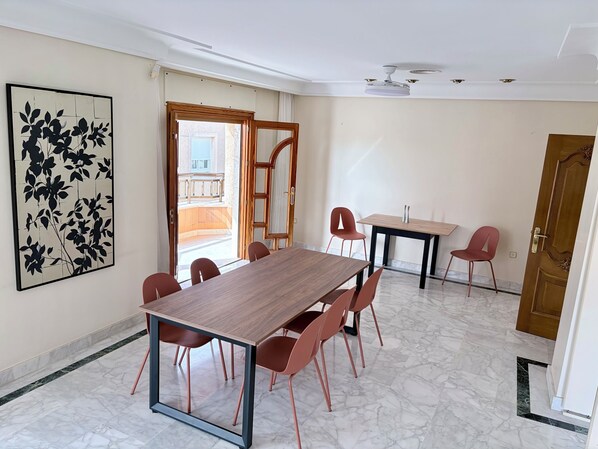 A dining area with a wooden table and red chairs, a ceiling fan, and a large floral artwork on the wall.