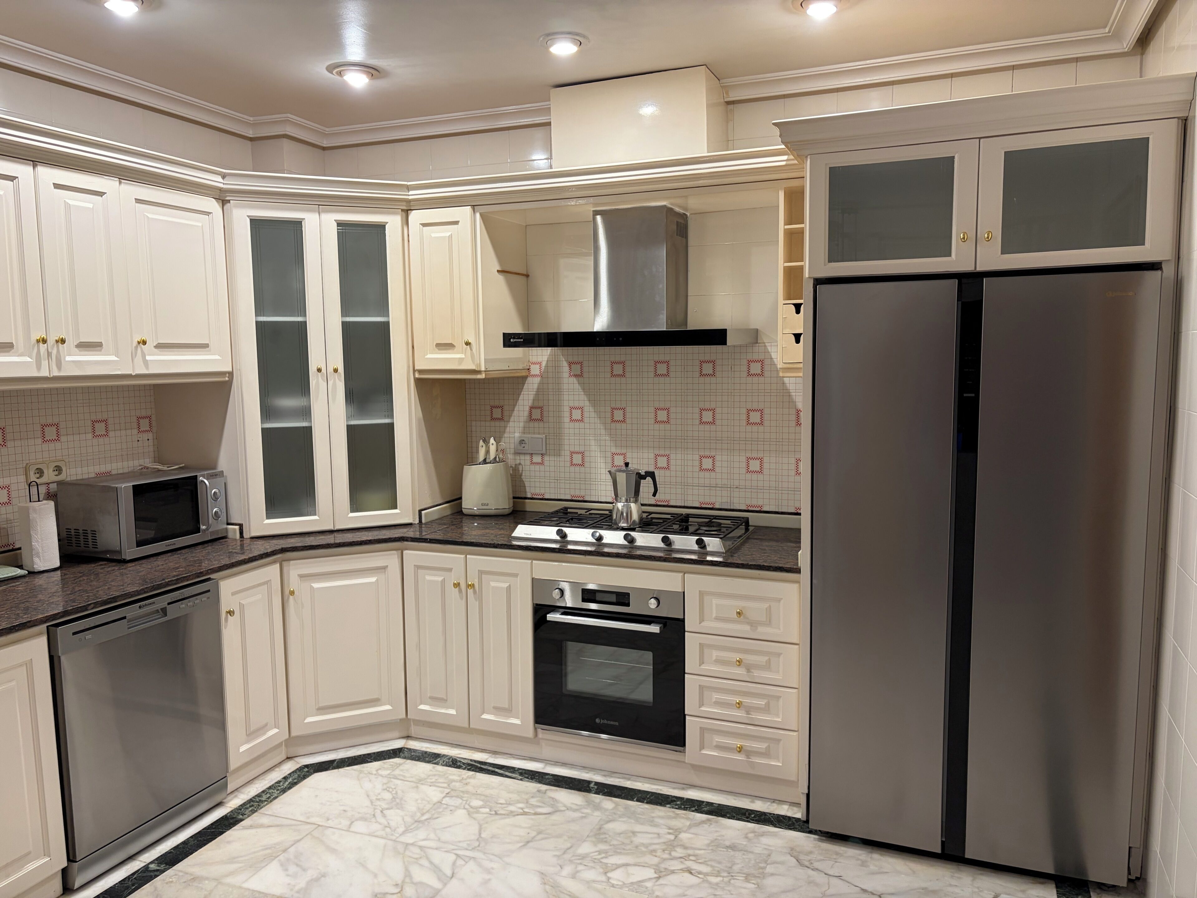 Una cocina moderna con armarios blancos, un refrigerador de acero inoxidable, horno empotrado, microondas y estufa a gas.