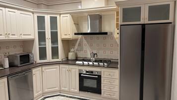 Una cocina moderna con armarios blancos, un refrigerador de acero inoxidable, horno empotrado, microondas y estufa a gas.
