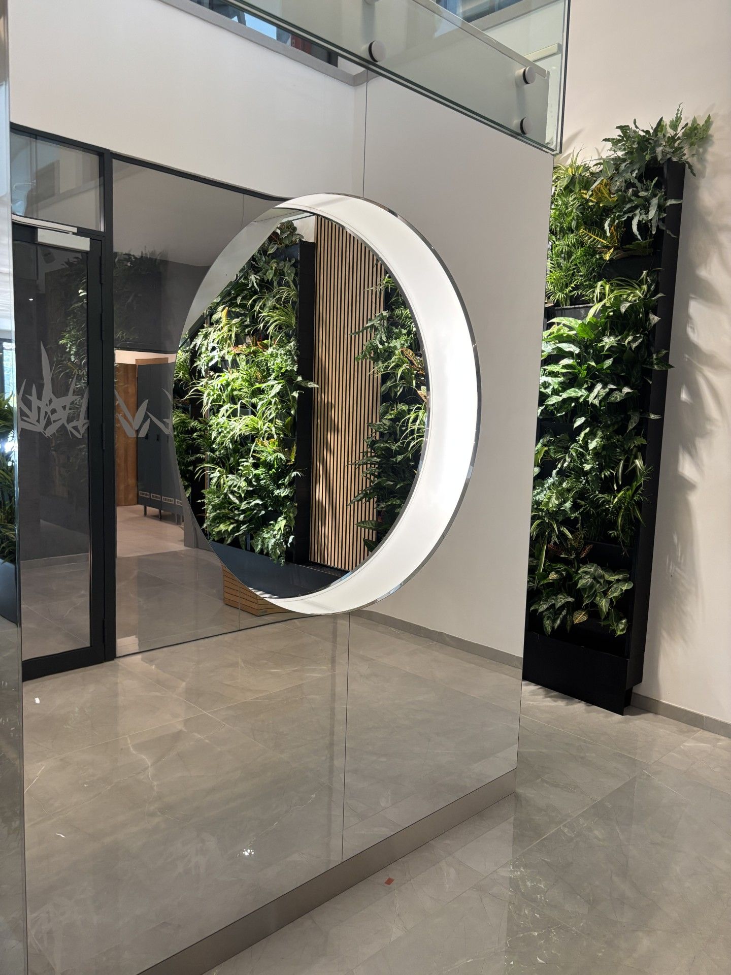A circular mirror with a wooden frame, reflecting a green wall with plants.