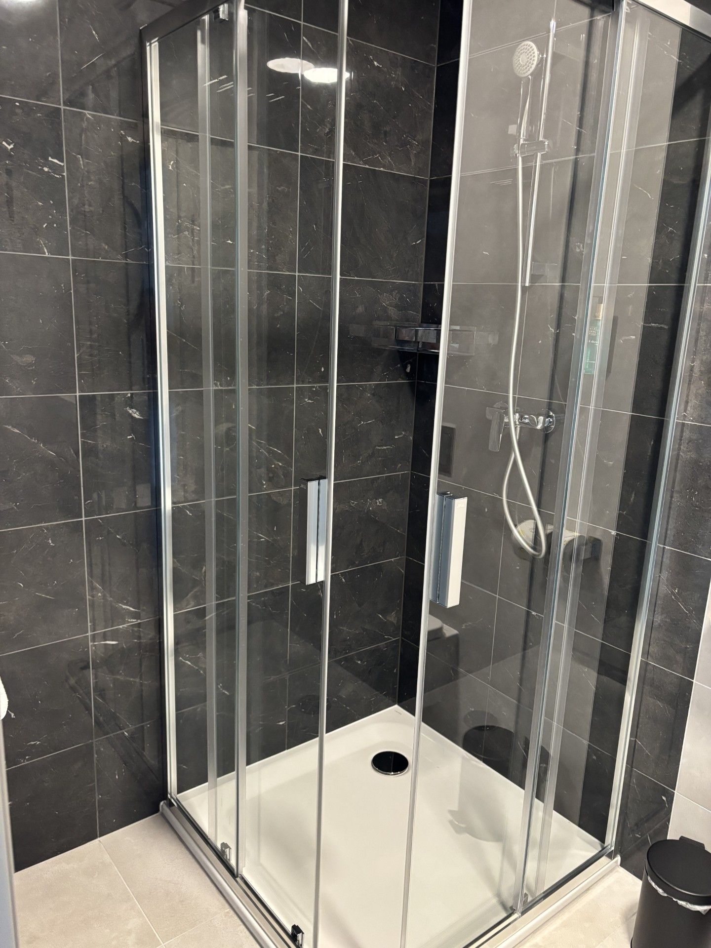 Cabina de ducha con paredes de mármol negro, piso blanco y ducha visible.