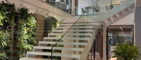 A modern interior with a glass staircase, indoor plants, and contemporary lighting fixtures.