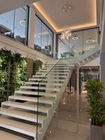 Un interior moderno con una escalera de cristal, plantas de interior e iluminación contemporánea.