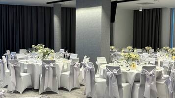 Ein Bankettraum mit runden Tischen, weißen Stühlen und floralen Tischdekorationen.