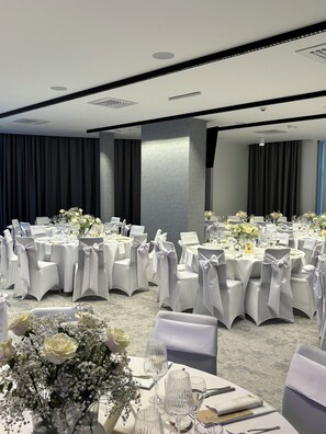 Un salón de banquetes con mesas redondas, sillas blancas y centros de mesa florales.