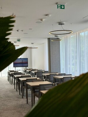 Un salón de conferencias con mesas y sillas, una pantalla grande y luces en el techo.