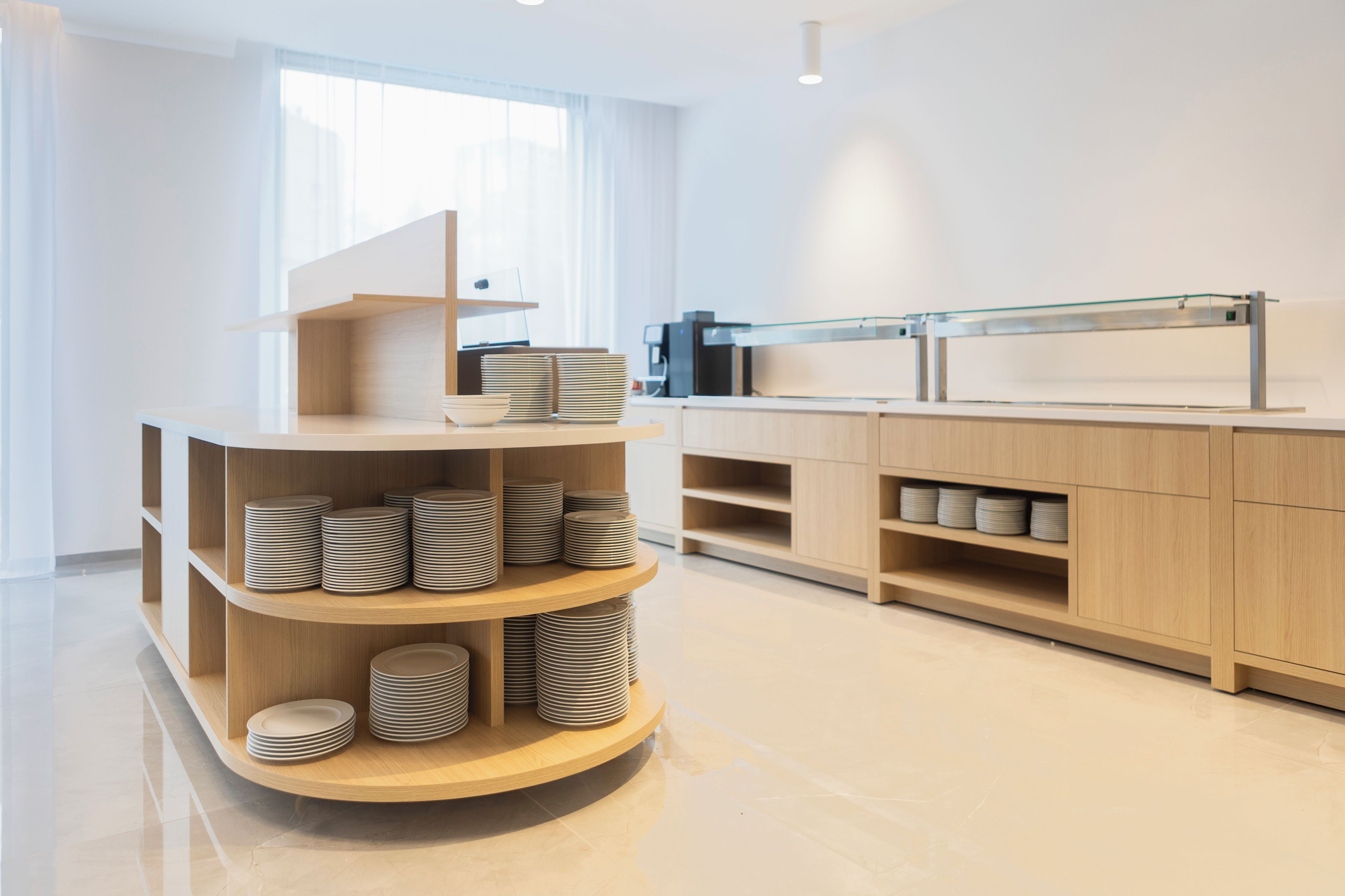 A modern kitchen with wooden cabinets, a glass display case, and neatly stacked plates.