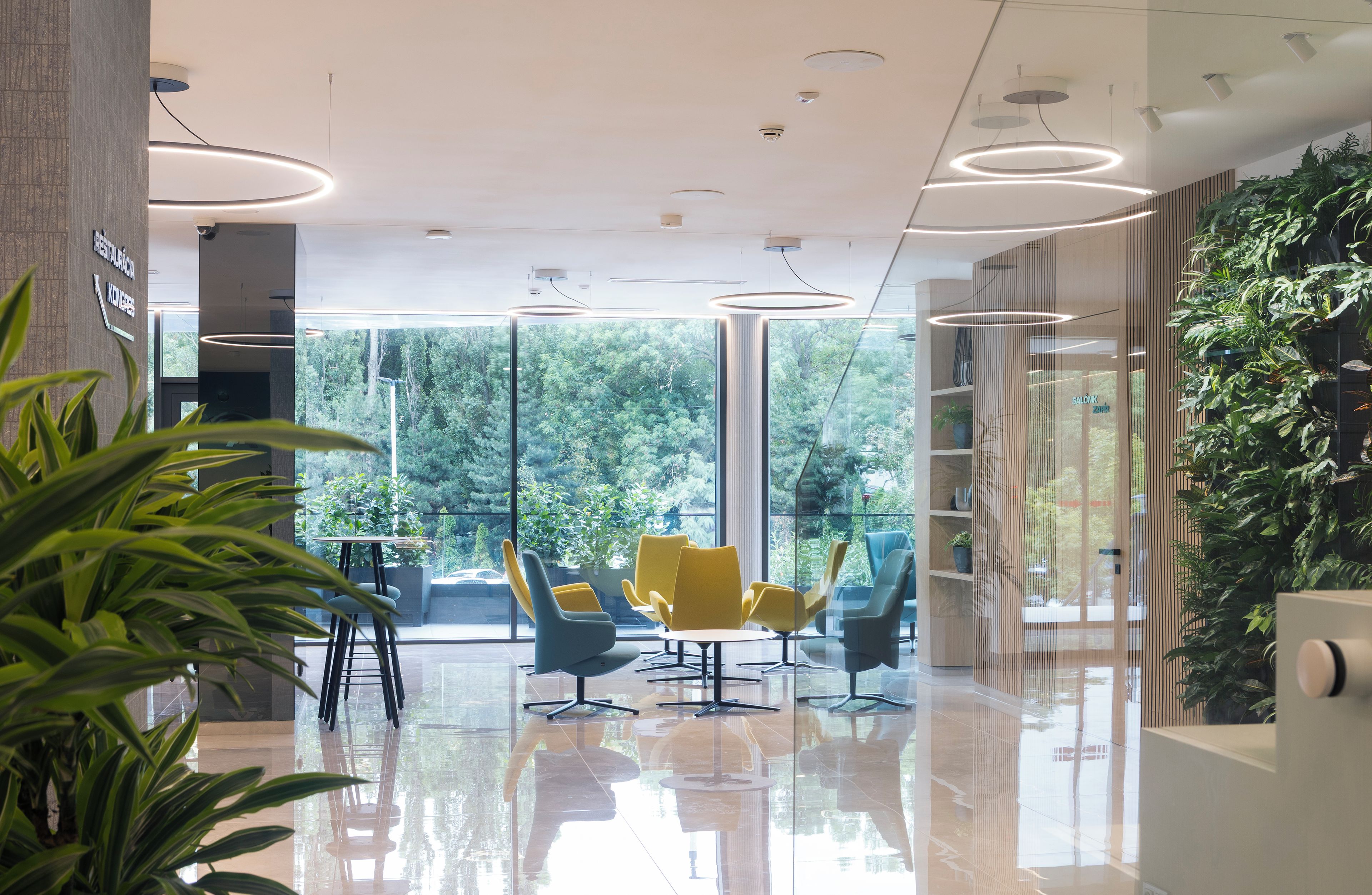 Ein modernes Interieur mit einer Glastrennwand, gelben Stühlen und Blick ins Grüne.