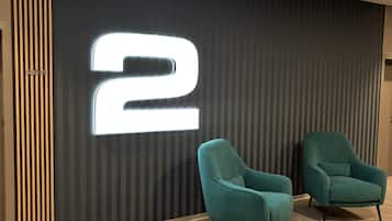 Un interior moderno con un número '2' iluminado en la pared, dos sillones color turquesa y un suelo estampado.