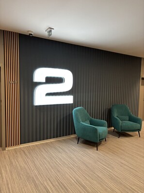 Un interior moderno con un número '2' iluminado en la pared, dos sillones color turquesa y un suelo estampado.