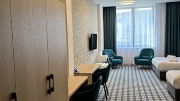 A hotel room with a checkered floor, a desk with chairs, a bed, and a TV mounted on the wall.