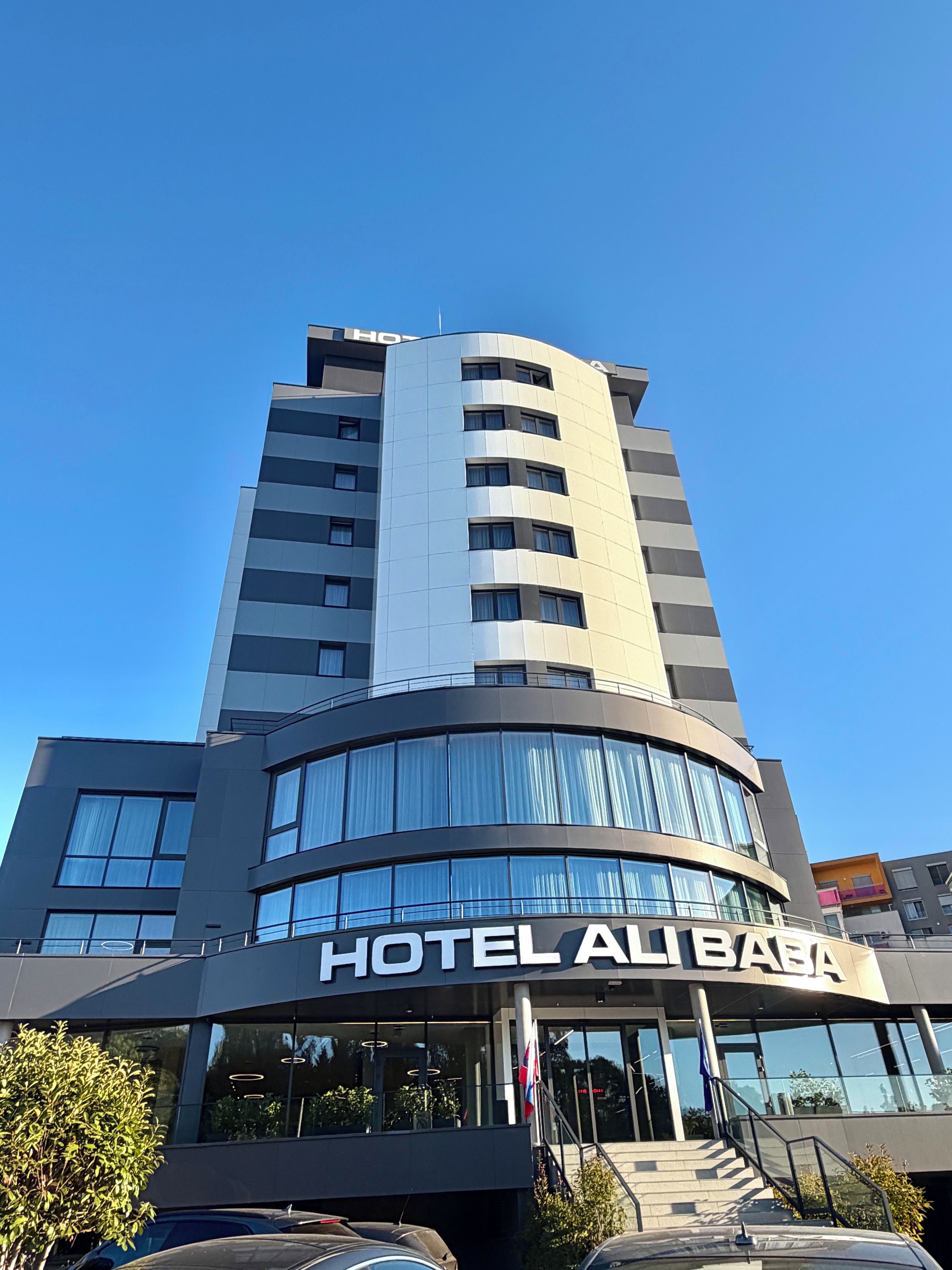 Un edificio de hotel moderno con fachada curva, ventanas amplias y un llamativo letrero 'HOTEL ALIBABA'.