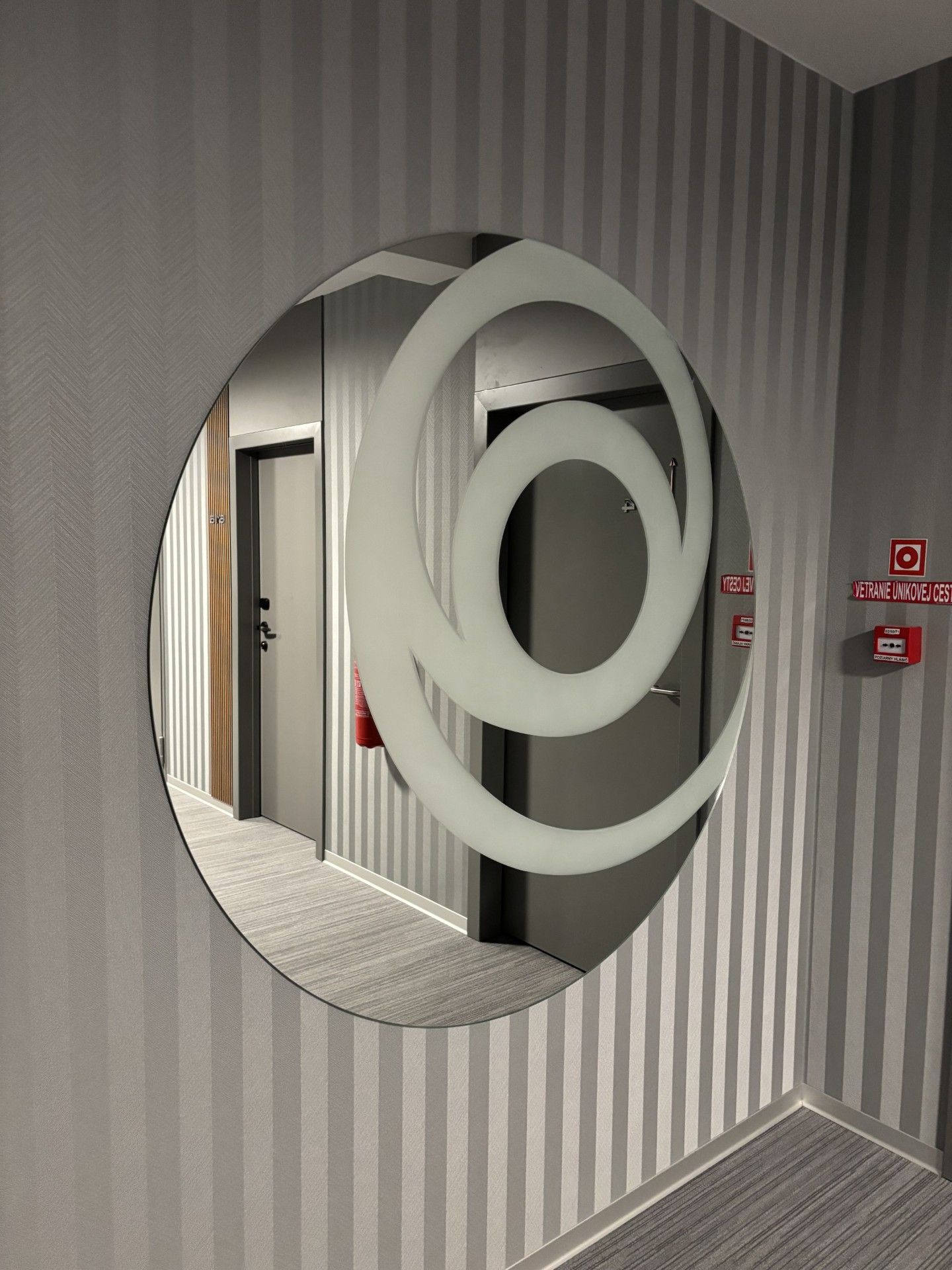 A hallway with a circular mirror on the wall, striped wallpaper, and a door with a fire alarm.