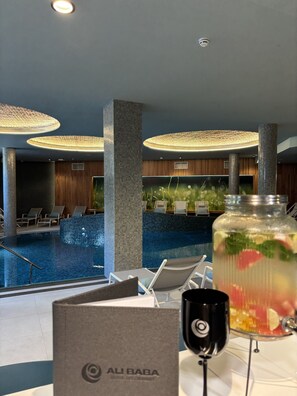 A pool area with lounge chairs, a glass table with a drink, and a sign reading 'AL BABA'.