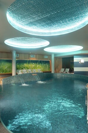 Una piscina interior con múltiples chorros de agua, sillones de descanso y una pared verde con exposición de plantas.