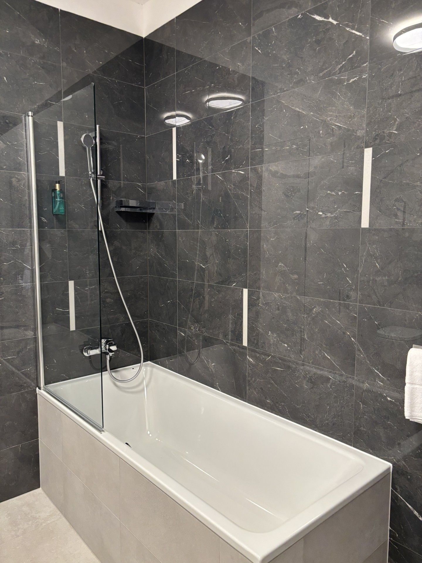 Ein modernes Badezimmer mit einer gläsernen Dusche, einer weißen Badewanne und dunklen Marmorwänden.