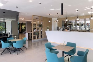 Zona de bar moderna con asientos y mostrador, rodeada de estanterías con plantas y botellas.