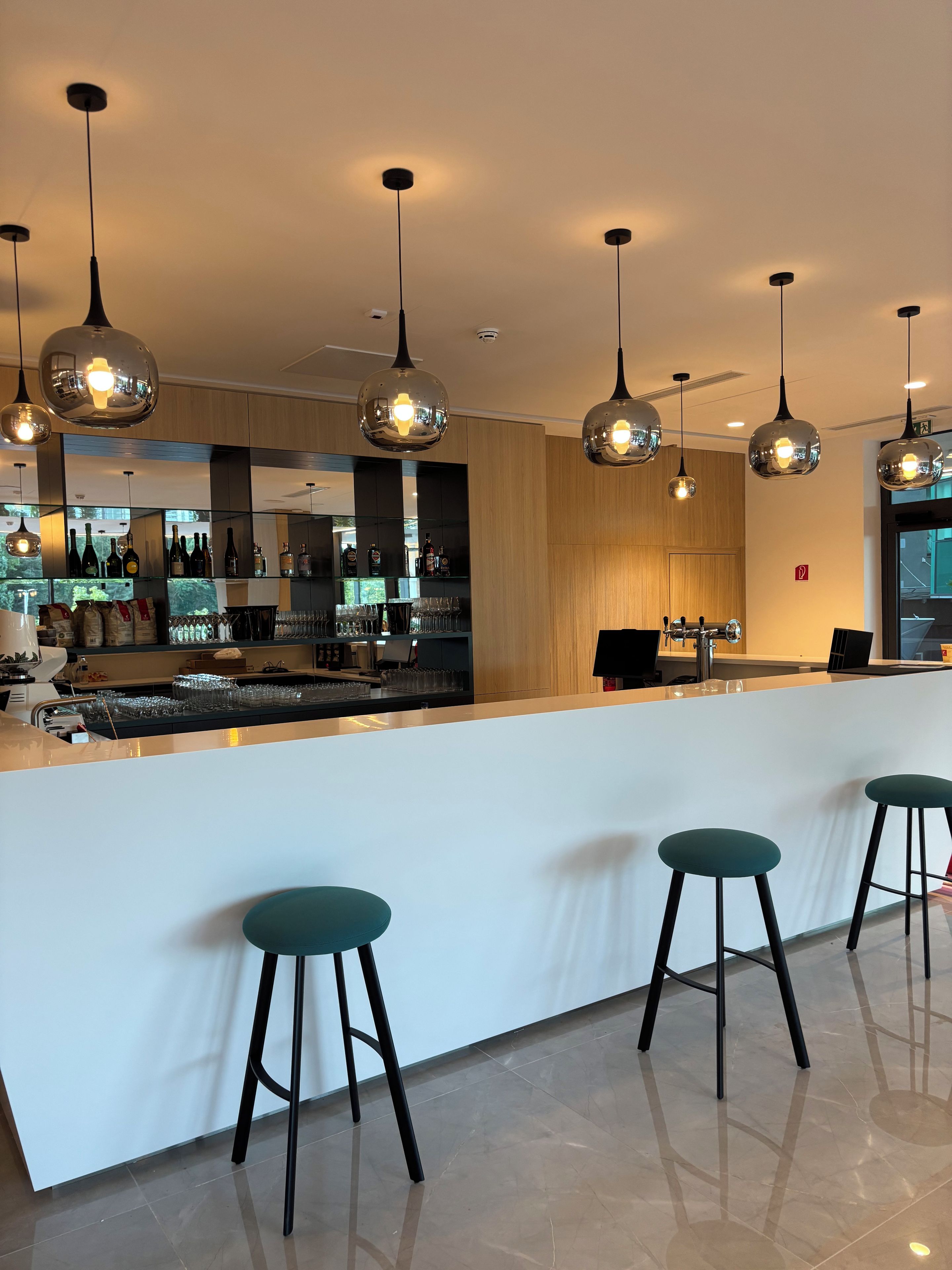 A modern bar area with a white counter, multiple hanging pendant lights, and bar stools.