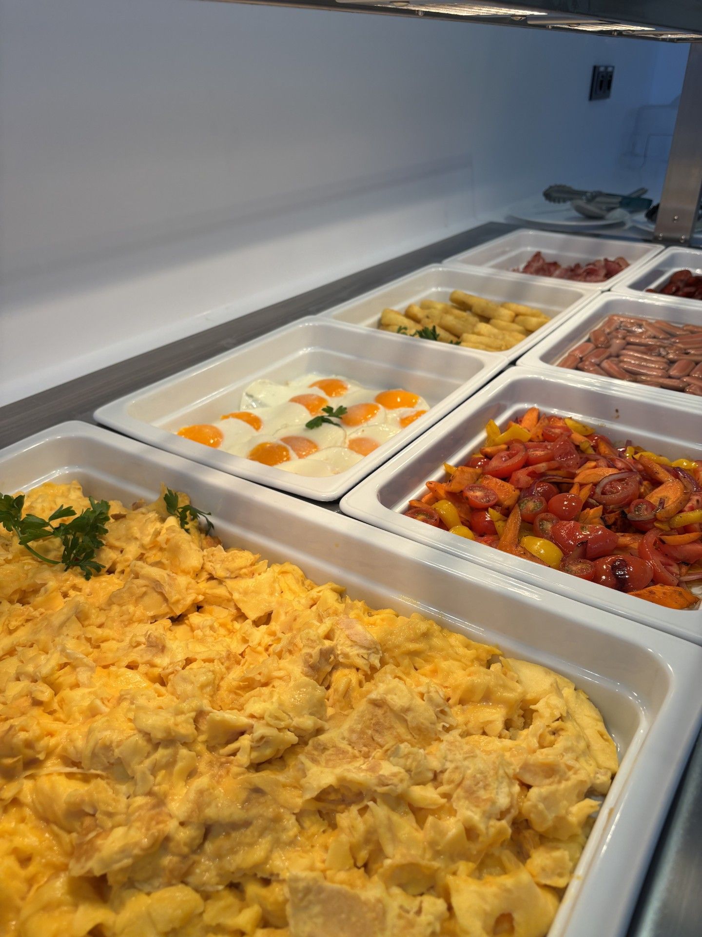 Ein reichhaltiges Buffet mit verschiedenen Speisen, darunter Rührei, Eier mit Orangenschnitten und einer Gemüsemischung.