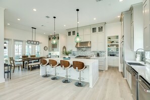 A modern kitchen with a central island, bar stools, pendant lighting, and a stone backsplash. - 2nd Row w/ Gulf Views in Beachside Village - All Suite Bedrooms+ Elevator (Galveston)