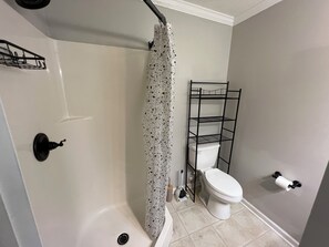 A bathroom with a shower, toilet, and a metal shelf unit.