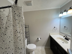 Een badkamer met een wit toilet, een wastafel met spiegel, een handdoekhouder en een douchegordijn met een puntpatroon.