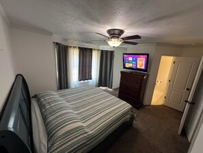 Een slaapkamer met een bed, een dressoir, een plafondventilator, een televisie en een deur.