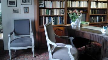 Une pièce avec deux chaises blanches, un bureau en bois, une bibliothèque remplie de livres et un tapis à motifs.