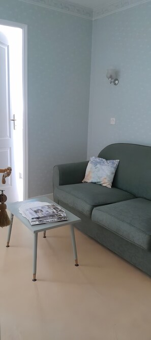 Un salon avec un canapé bleu clair, une petite table avec des magazines et une porte dotée d’une poignée.