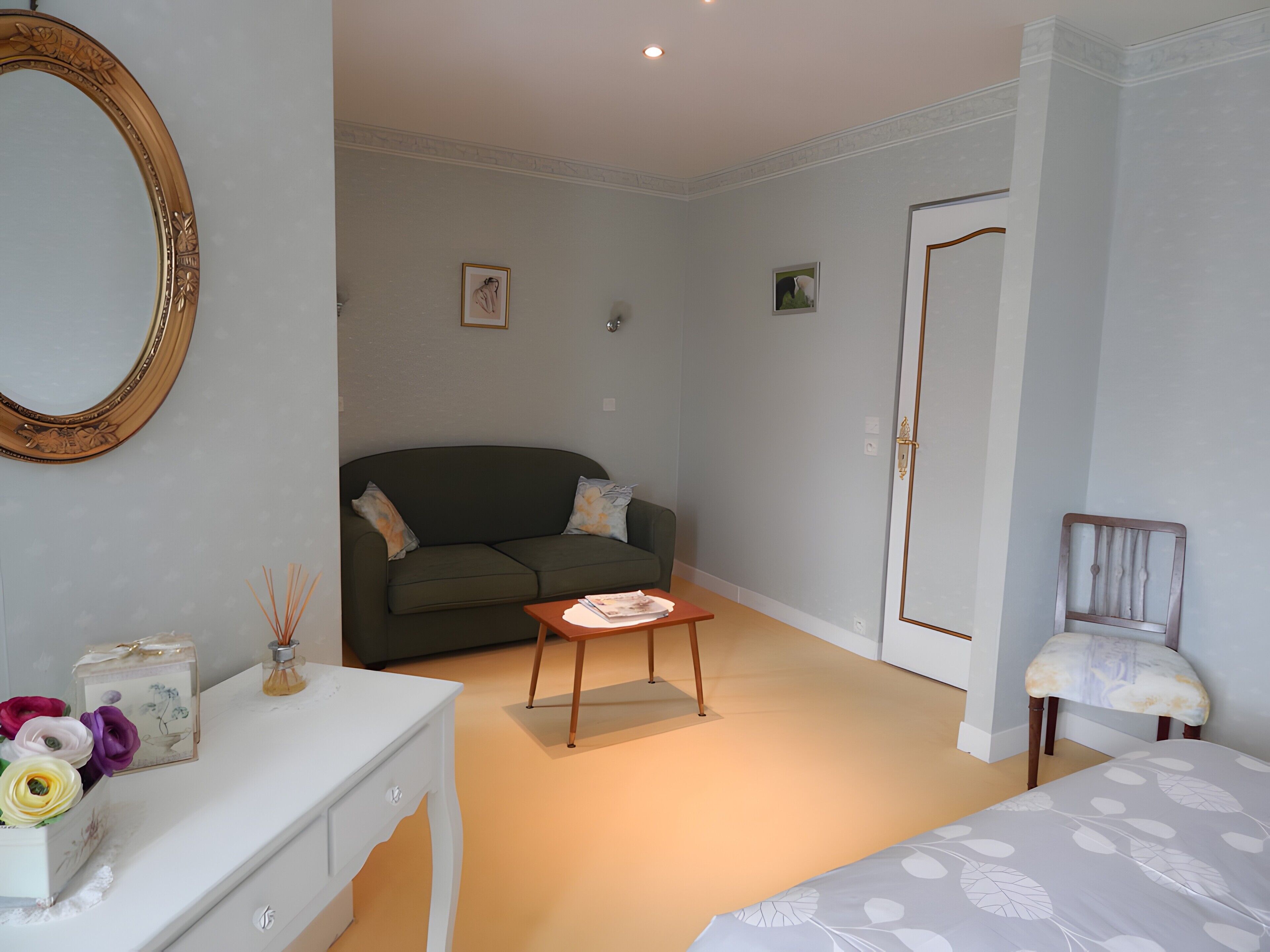 Une pièce avec un canapé vert, une commode blanche, une petite table, une chaise et une porte.