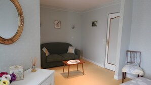 A room with a green sofa, a white dresser, a small table, a chair, and a door.