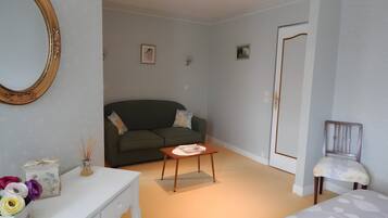 Une pièce avec un canapé vert, une commode blanche, une petite table, une chaise et une porte.