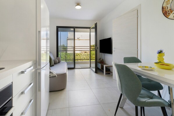 A modern kitchen with a dining area, a balcony with a view, and a flat-screen TV mounted on the wall.