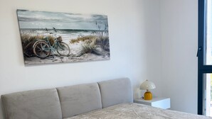 A bedroom with a bed, a nightstand, a lamp, and a painting of a beach scene.